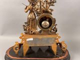 a gold clock on a marble base with a lady and a man
