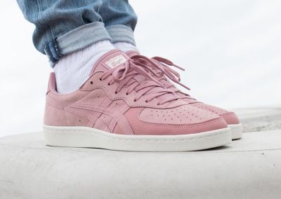 Une personne se tient sur un rebord, vêtue d'un jean et de baskets roses.