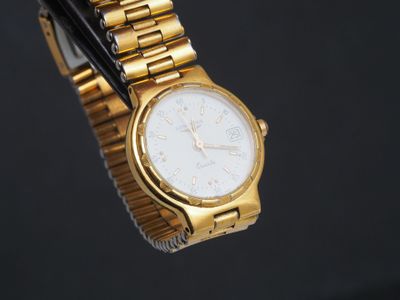 une montre en or avec un cadran blanc sur fond noir