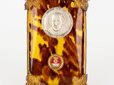 une photo d'une petite horloge en écaille de tortue sur laquelle repose une pièce de monnaie