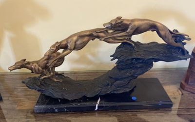 a bronze sculpture of a dog leaping over a rock