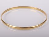 gros plan d'un bracelet en or sur une surface blanche