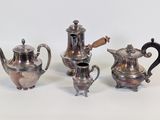 three silver teapots and a coffee pot on a white surface