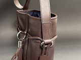brown leather bucket bag with tassels on a grey background