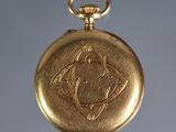a gold pocket watch that has a picture of a bird on it