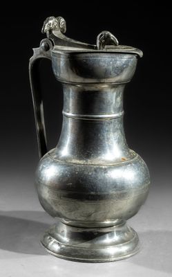 an old silver pitcher with a handle on a white surface