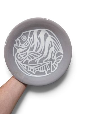 une main tenant une assiette ornée d'un motif de poisson
