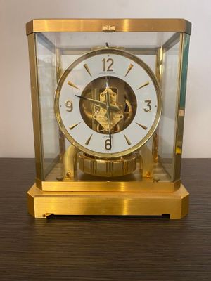 a gold clock sitting on a wooden table with a white wall in the background
