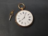 une montre de poche en or et une clé posées sur une table