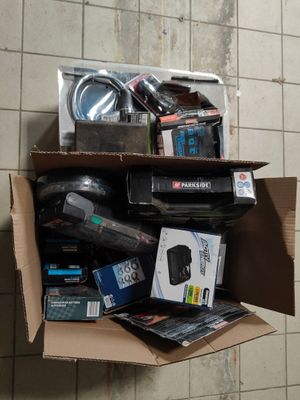 une boîte en carton remplie d'appareils électroniques divers, posée sur un sol carrelé
