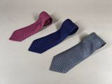 three ties are lined up on a white surface, one is blue and the other is pink