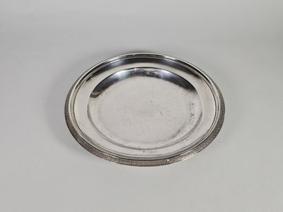 une assiette en argent posée sur une table blanche, avec une tasse à l'arrière-plan