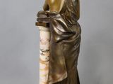 a bronze statue of a woman reading a book on a marble column