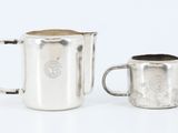 une image représentant un pichet et une coupe en argent posés sur une surface blanche