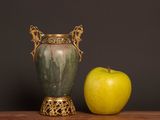 a green vase next to an apple on a table