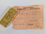 un lingot d'or et un reçu posés sur une table blanche, sur fond blanc