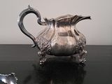a silver pitcher sitting on a table with a spoon in front of it