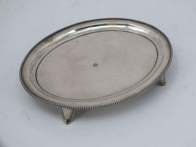 an oval silver tray with a beaded edge on a white surface