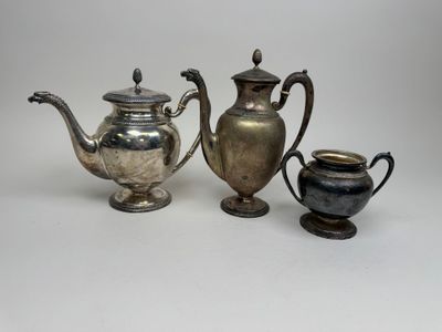 two silver teapots and a silver cup on a white surface