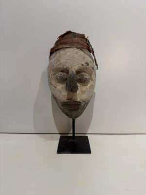 a wooden mask on a black stand on a white wall