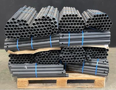 pile de tuyaux noirs empilés sur une palette devant un mur noir