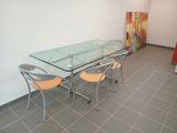 une table et des chaises en verre dans une pièce où est accroché un tableau au mur