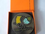 une boîte orange contenant une médaille d'argent, posée sur une surface blanche