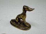 brass dog figurine sitting on top of a coin on a white surface
