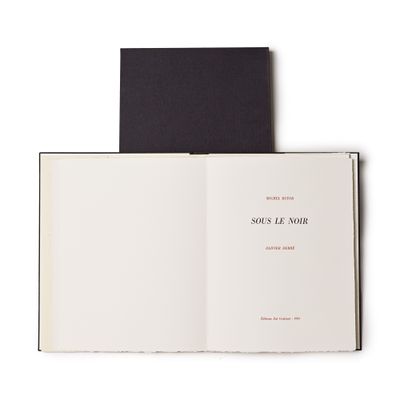 un livre ouvert posé sur une table blanche, à côté d'un livre noir