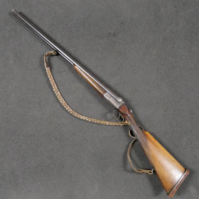 un fusil avec une crosse en bois et une chaîne, posé sur une surface grise