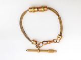 a close up of a gold bracelet with a bullet on a white background