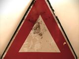 un panneau triangulaire rouge et blanc sur un mur blanc
