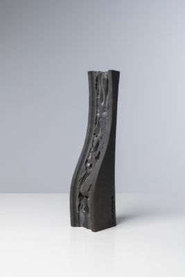 sculpture représentant un bloc de bois noir incurvé posé sur une surface blanche