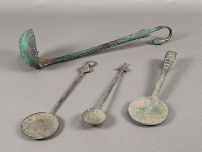 trois vieilles cuillères en métal et un repose-cuillère posés sur une table