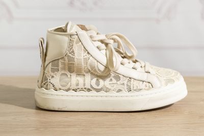beige lace high top sneakers on a wooden surface with a white background