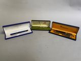 trois stylos se trouvent dans une boîte posée sur une table, sur fond blanc