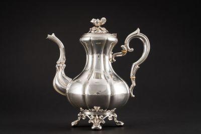 une cafetière ancienne en argent posée sur un support, sur fond noir