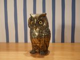 an owl figurine sitting on a table in front of a striped wall