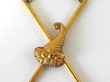 une image représentant une broche plaquée or ornée de deux bâtons croisés et d'une boule