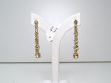 une paire de boucles d'oreilles dorées posées sur un présentoir blanc, sur une table