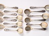 six cuillères en argent sont disposées en ligne sur une surface blanche