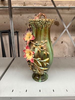 a green vase with flowers on it sitting on a shelf