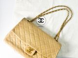 un sac Chanel beige avec une bandoulière en chaîne dorée posé sur un sac blanc