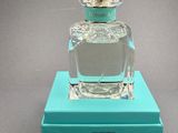 the bottle of perfume is sitting on a blue box on a gray surface