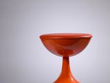 an orange vase sitting on top of a white table next to a gray wall