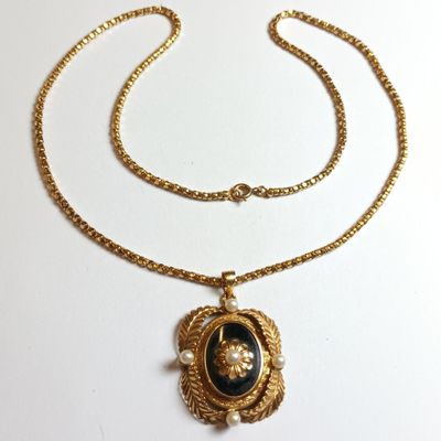 un collier en or avec un pendentif noir et blanc suspendu à une chaîne en or