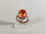 a ring with an orange stone in it on a clear stand