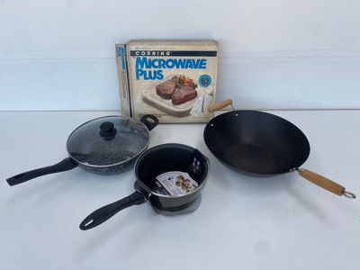 trois casseroles et poêles posées sur une table à côté d'un carton « Microwave Plus »