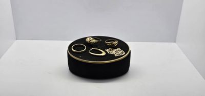 une boîte noire ornée d'anneaux dorés, posée sur une surface blanche