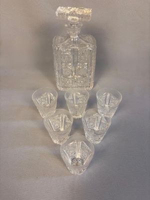 une carafe en verre et six verres posés sur une table